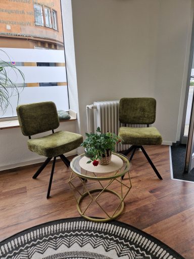 Zwei grüne Sessel mit einem runden Kaffeetisch und einer Pflanze in einem modernen Raum.